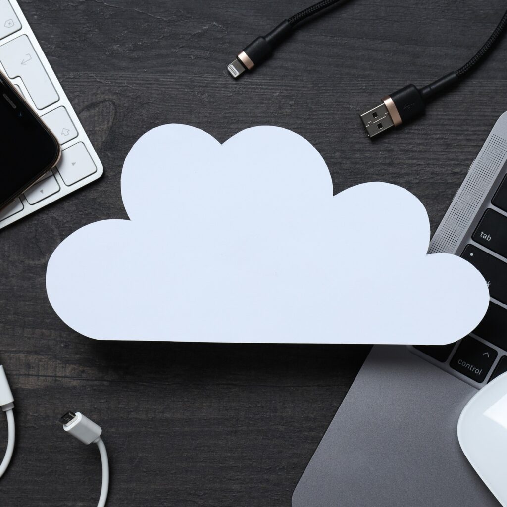 White, paper cloud with various gadgets on a black table background