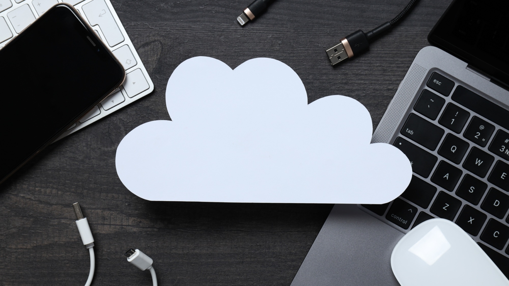 White, paper cloud with various gadgets on a black table background