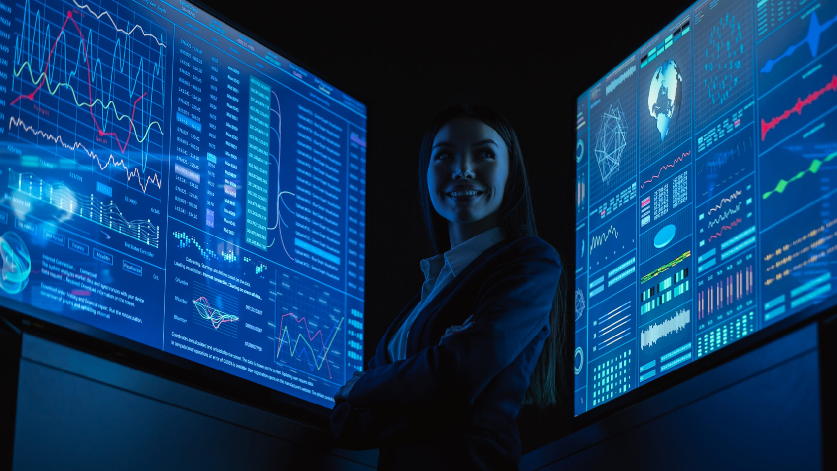 The smiling business lady standing between blue monitors in the dark office