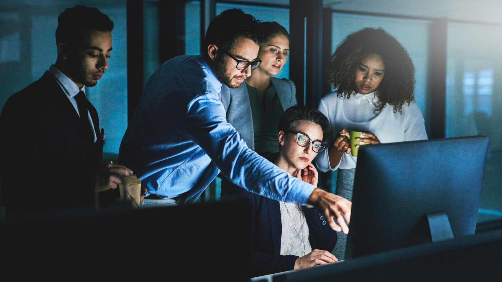 Shot of colleagues standing together as they work on something on a computer at night.
