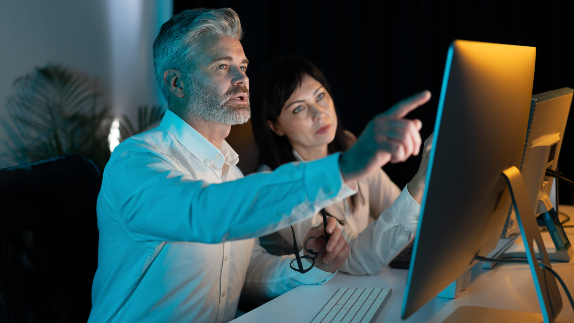 Two Business Professionals Collaborating At Computer In Office, Analyzing Data And Discussing Project, Focused And Engaged, Teamwork And Collaboration Concept In Modern Workplace Setting